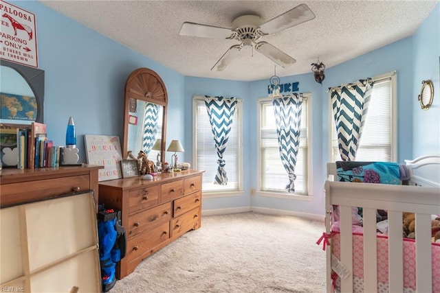 bedroom featuring ceiling fan, a textured ceiling, a nursery area, and carpet floors