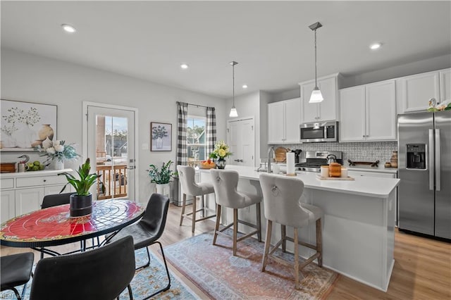 kitchen featuring decorative light fixtures, light hardwood / wood-style floors, a center island with sink, appliances with stainless steel finishes, and white cabinets