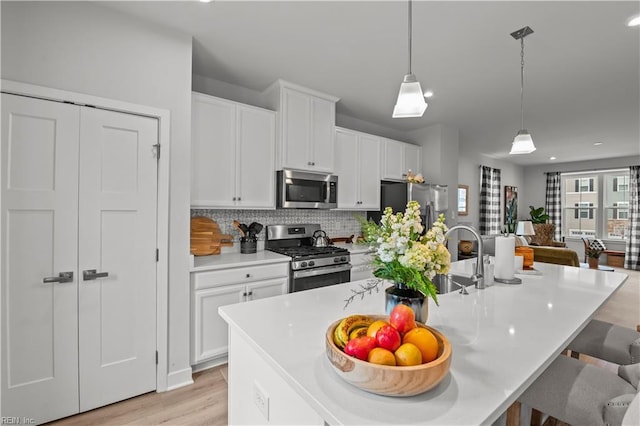 kitchen with appliances with stainless steel finishes, tasteful backsplash, decorative light fixtures, and a kitchen island with sink