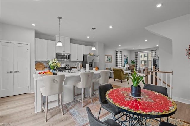 kitchen with backsplash, a center island with sink, hanging light fixtures, stainless steel appliances, and white cabinets