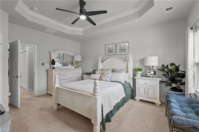 bedroom with ceiling fan, light colored carpet, and a tray ceiling