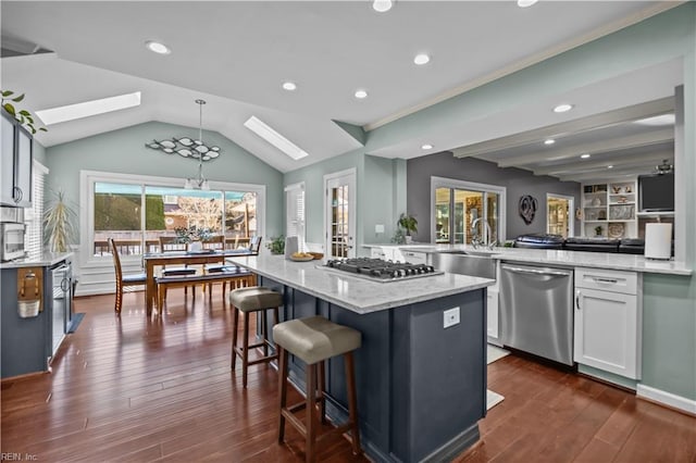 kitchen featuring dark wood-type flooring, stainless steel appliances, light stone countertops, white cabinets, and a kitchen island