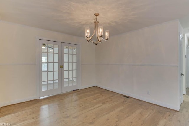 spare room featuring a chandelier, light hardwood / wood-style flooring, and french doors