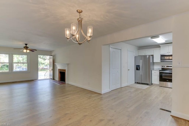 unfurnished living room featuring ceiling fan with notable chandelier, light hardwood / wood-style flooring, and a fireplace