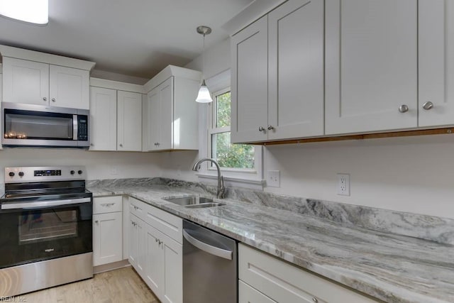 kitchen featuring white cabinetry, appliances with stainless steel finishes, decorative light fixtures, light stone countertops, and sink