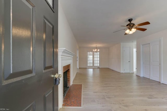 living room with light wood-type flooring, a fireplace, and ceiling fan with notable chandelier