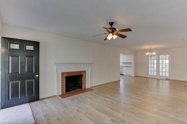 unfurnished living room with a brick fireplace, light hardwood / wood-style floors, ceiling fan with notable chandelier, and french doors