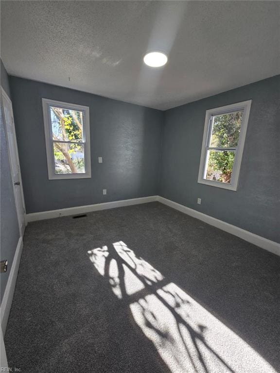 unfurnished room with a textured ceiling and dark colored carpet