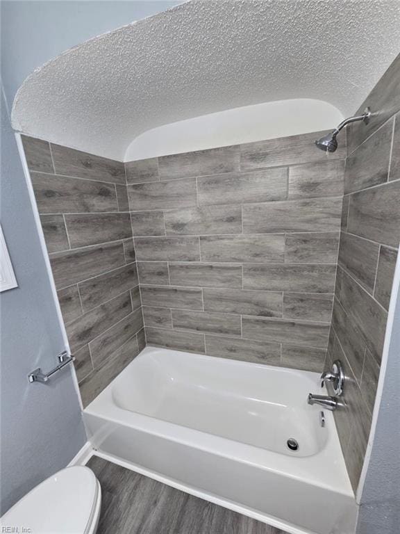 bathroom featuring toilet, tiled shower / bath combo, wood-type flooring, and a textured ceiling