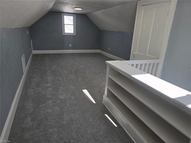 additional living space featuring dark carpet, a textured ceiling, and vaulted ceiling