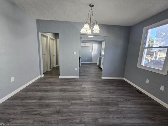 unfurnished dining area featuring dark wood-type flooring, a textured ceiling, and an inviting chandelier