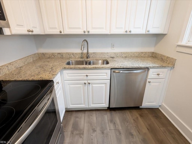 kitchen with appliances with stainless steel finishes, wood-type flooring, white cabinets, light stone counters, and sink