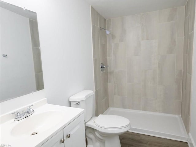 bathroom with toilet, tiled shower, hardwood / wood-style floors, and vanity