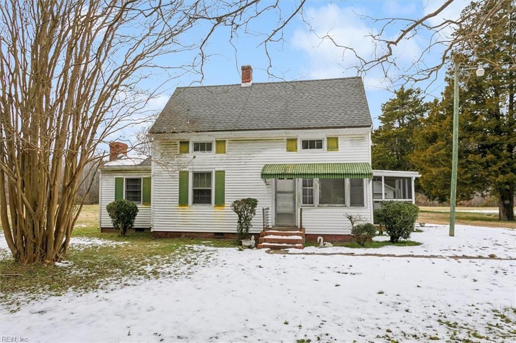 snow covered back of property featuring a sunroom