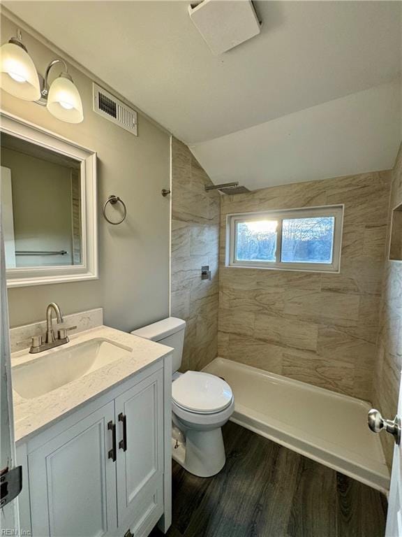 bathroom with hardwood / wood-style floors, lofted ceiling, vanity, toilet, and a tile shower