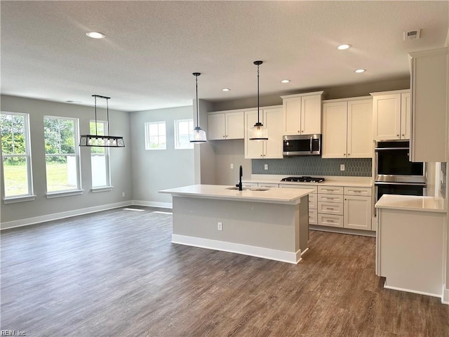 kitchen featuring decorative light fixtures, white cabinets, stainless steel appliances, and a kitchen island with sink