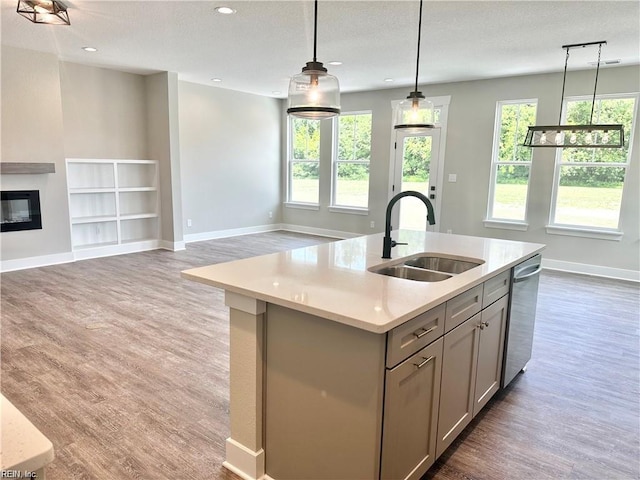 kitchen with gray cabinetry, a kitchen island with sink, hanging light fixtures, stainless steel dishwasher, and sink