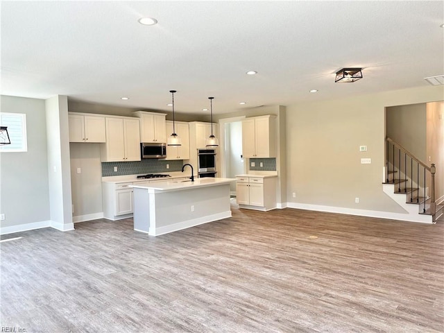 kitchen featuring decorative light fixtures, light hardwood / wood-style floors, a center island with sink, stainless steel appliances, and white cabinets