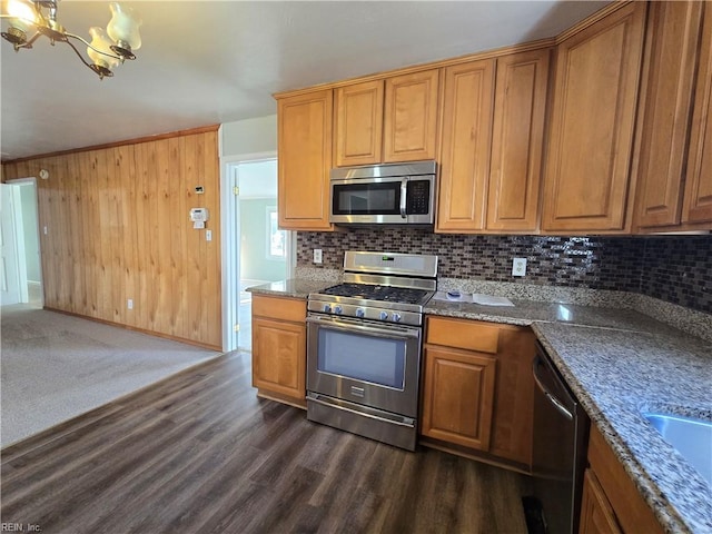 kitchen with an inviting chandelier, appliances with stainless steel finishes, decorative light fixtures, dark wood-type flooring, and dark stone countertops