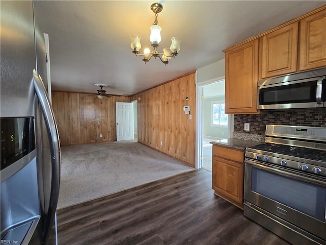 kitchen with ceiling fan with notable chandelier, stainless steel appliances, dark stone counters, dark colored carpet, and hanging light fixtures