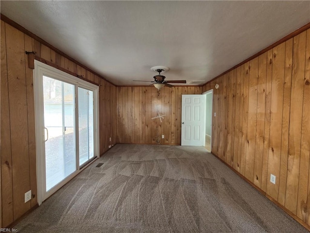 carpeted spare room featuring ceiling fan and wooden walls