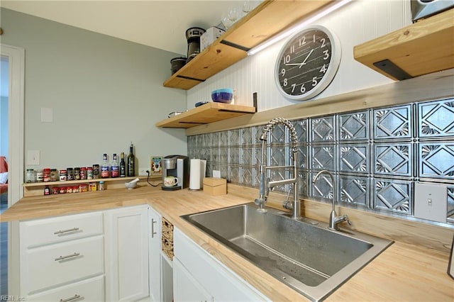 kitchen with decorative backsplash, wooden counters, sink, and white cabinetry