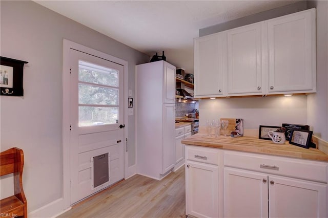 kitchen with wall chimney exhaust hood, wood counters, white cabinetry, light hardwood / wood-style floors, and stainless steel stove