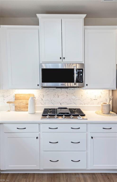 kitchen with dark wood-type flooring, stainless steel appliances, white cabinetry, and tasteful backsplash