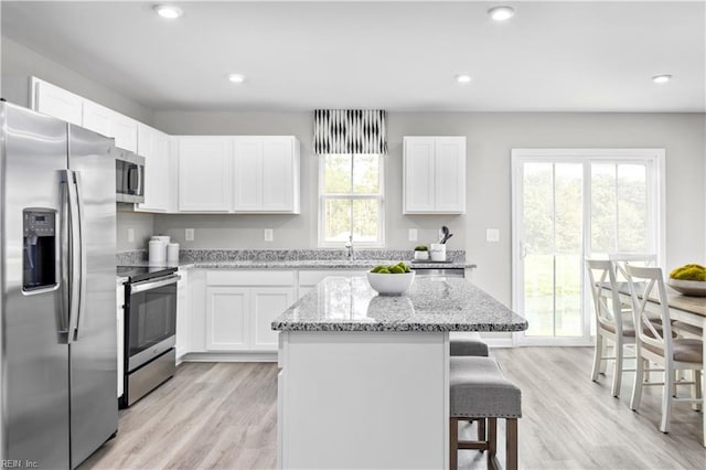 kitchen with appliances with stainless steel finishes, a kitchen breakfast bar, light stone countertops, white cabinets, and a center island