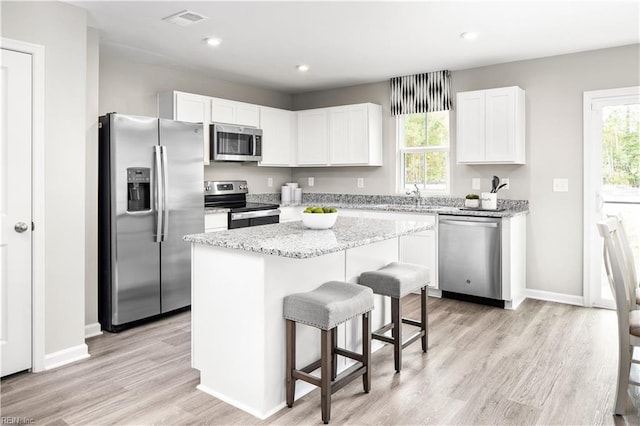 kitchen with stainless steel appliances, a healthy amount of sunlight, white cabinets, a kitchen island, and light hardwood / wood-style flooring