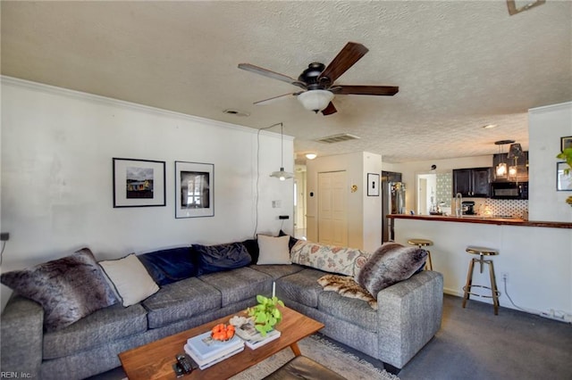 living room featuring ceiling fan, dark carpet, a textured ceiling, and ornamental molding