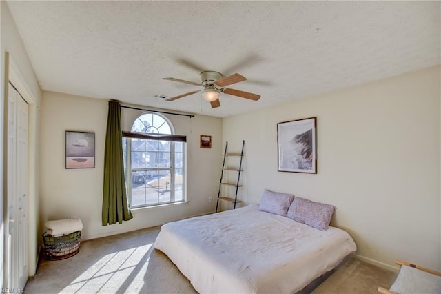 bedroom with a textured ceiling, ceiling fan, a closet, and light colored carpet