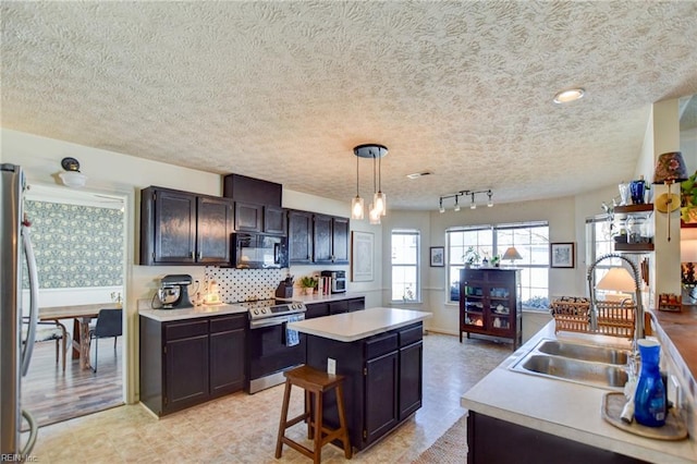 kitchen featuring stainless steel appliances, backsplash, decorative light fixtures, a kitchen island, and sink