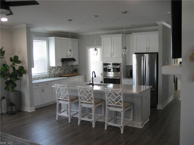 kitchen with sink, decorative light fixtures, appliances with stainless steel finishes, a kitchen island with sink, and white cabinets