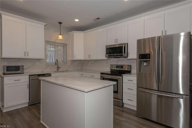 kitchen with appliances with stainless steel finishes, a center island, decorative light fixtures, white cabinetry, and tasteful backsplash