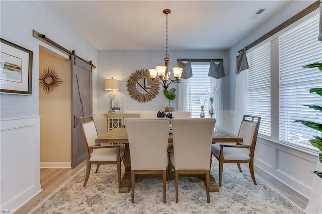 dining area with a chandelier, a barn door, and light hardwood / wood-style flooring