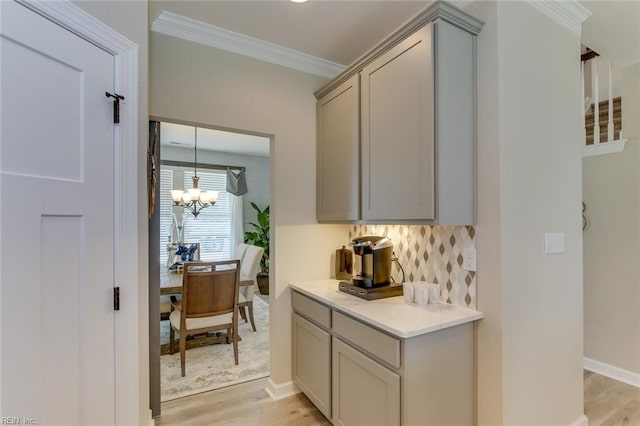 bar featuring tasteful backsplash, light hardwood / wood-style floors, an inviting chandelier, ornamental molding, and gray cabinetry