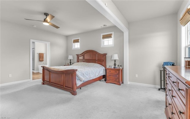 bedroom featuring ceiling fan, light colored carpet, and ensuite bath