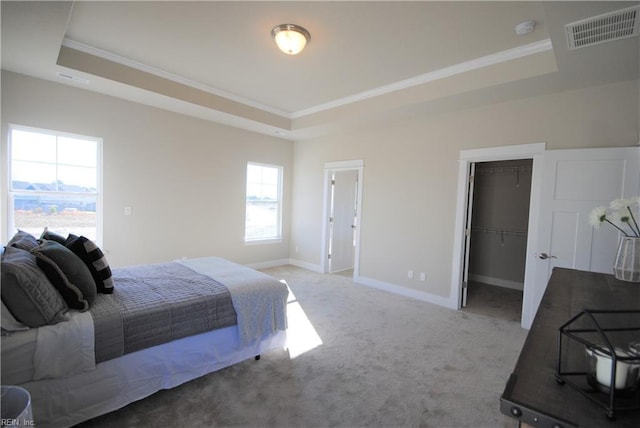 carpeted bedroom featuring a walk in closet, a closet, a tray ceiling, and ornamental molding