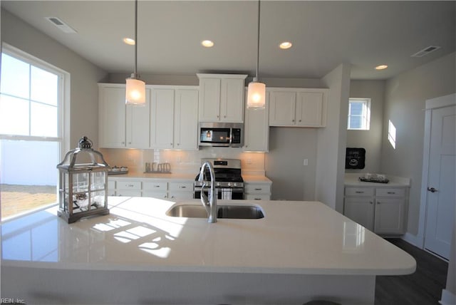 kitchen featuring appliances with stainless steel finishes, an island with sink, white cabinets, and decorative light fixtures