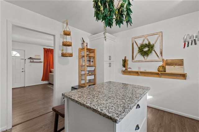 kitchen with a center island, light stone countertops, white cabinetry, and dark hardwood / wood-style floors