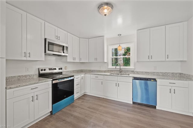 kitchen featuring appliances with stainless steel finishes, white cabinetry, sink, hanging light fixtures, and light wood-type flooring