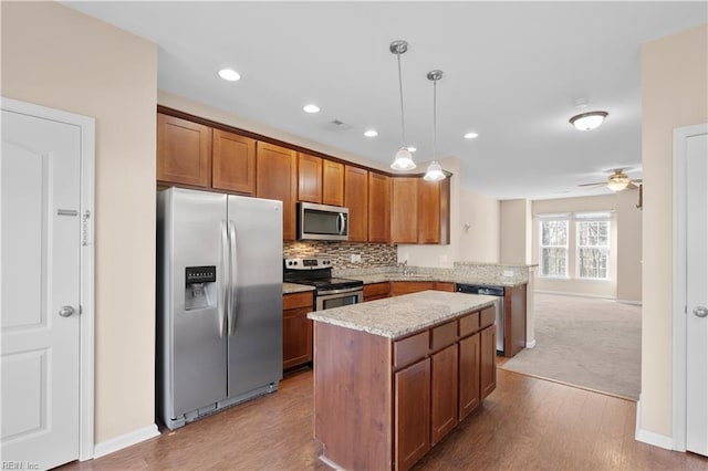 kitchen featuring ceiling fan, light hardwood / wood-style floors, hanging light fixtures, appliances with stainless steel finishes, and light stone countertops