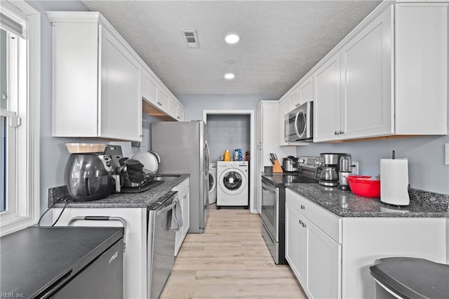 kitchen featuring a textured ceiling, stainless steel appliances, washer and clothes dryer, and white cabinets