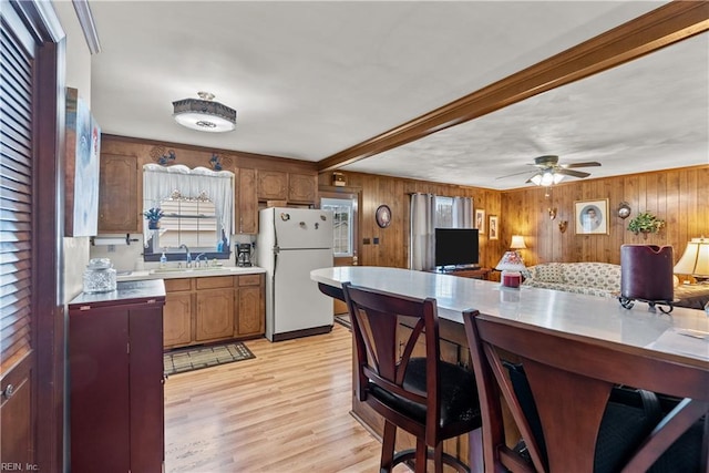 kitchen featuring white refrigerator, wooden walls, sink, ceiling fan, and light hardwood / wood-style flooring