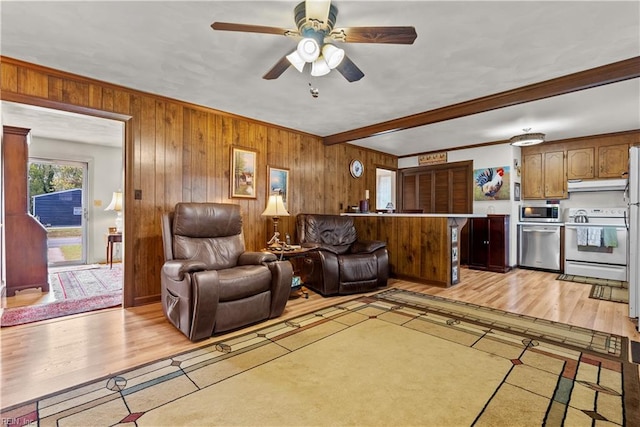 living room featuring ceiling fan, crown molding, light hardwood / wood-style floors, and wood walls