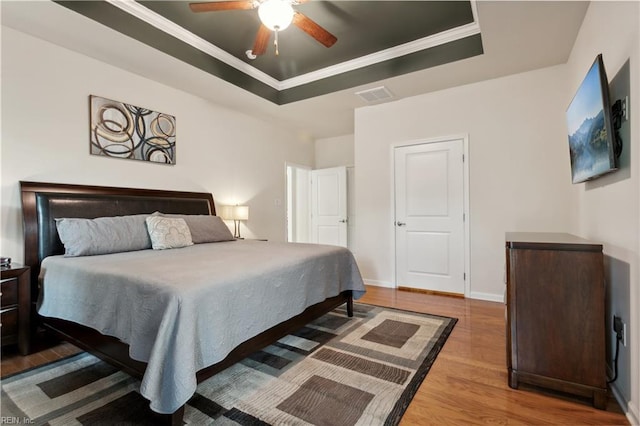 bedroom with ceiling fan, hardwood / wood-style floors, crown molding, and a raised ceiling