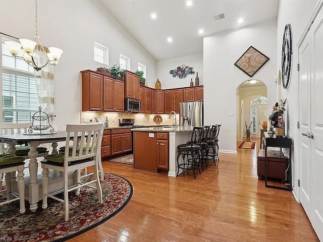 kitchen featuring tasteful backsplash, a breakfast bar, a towering ceiling, a kitchen island with sink, and stainless steel appliances