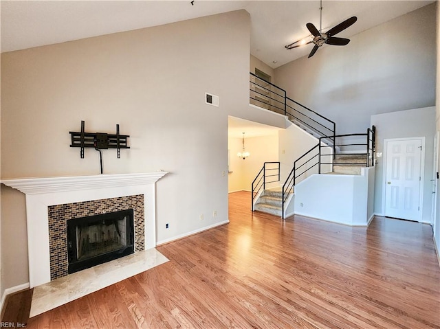 unfurnished living room with ceiling fan, a tile fireplace, high vaulted ceiling, and light hardwood / wood-style flooring