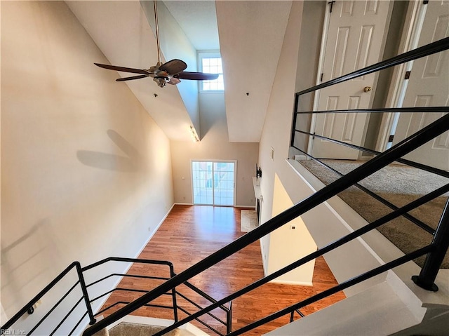 stairway with ceiling fan, a towering ceiling, and hardwood / wood-style floors